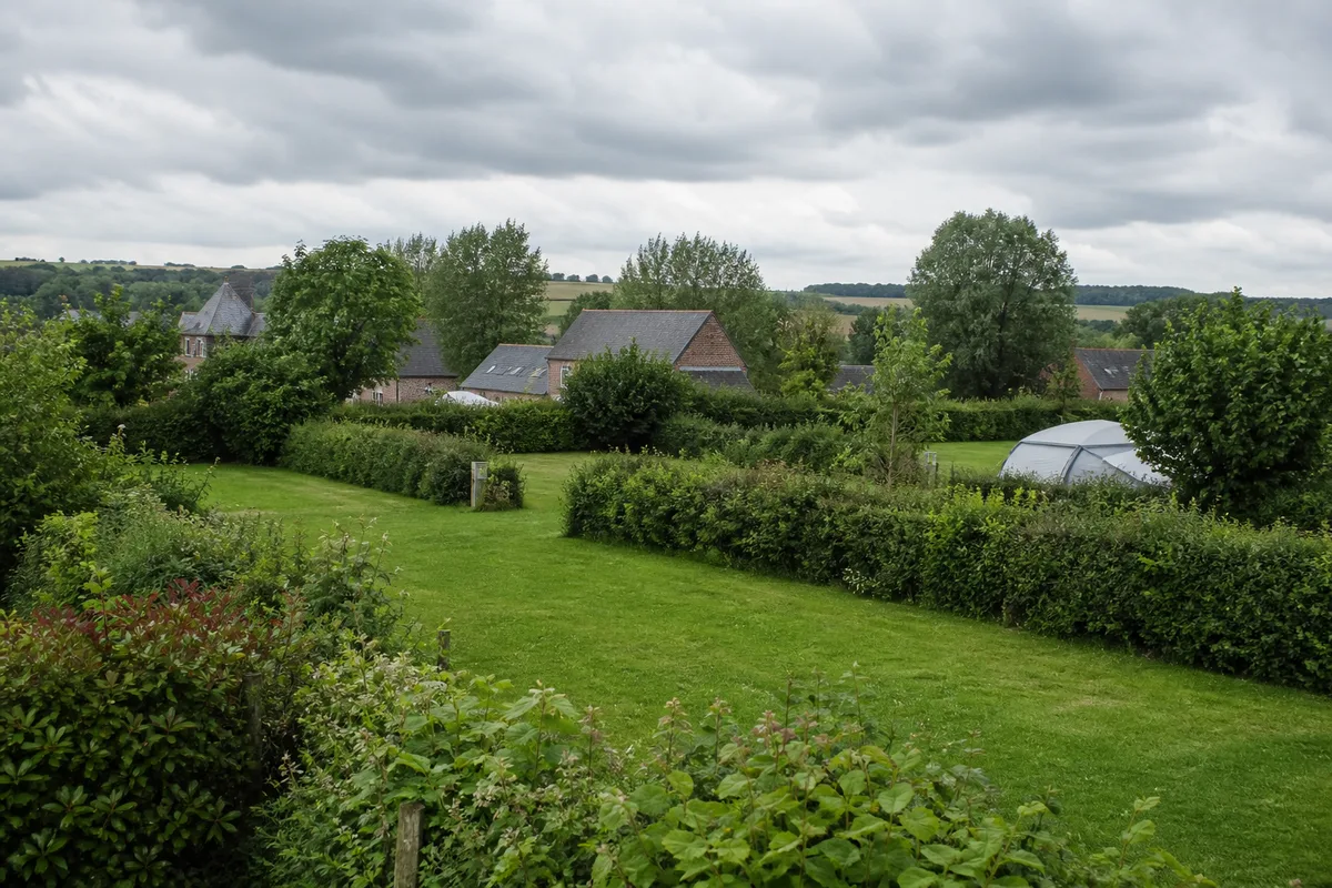 Emplacements de camping en herbe entourés de haies bocagères sous un ciel couvert